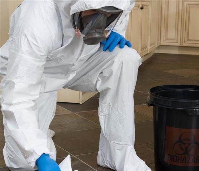 Person in biohazard suit and mask, cleaning a floor